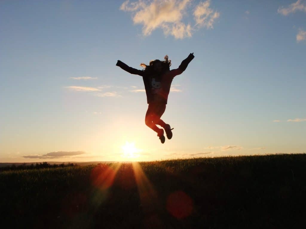 Photo d'un enfant qui saute en l'air devant un coucher de soleil pour représenter le succès vers lequel le coach vous amène.